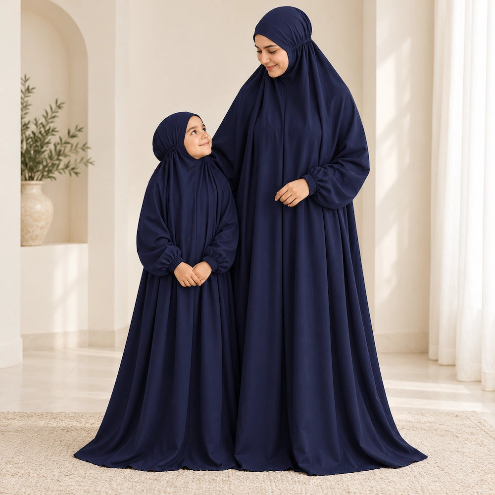 Daughter looking up at her mother while both wear matching solid navy blue full-length namaz chaddars.