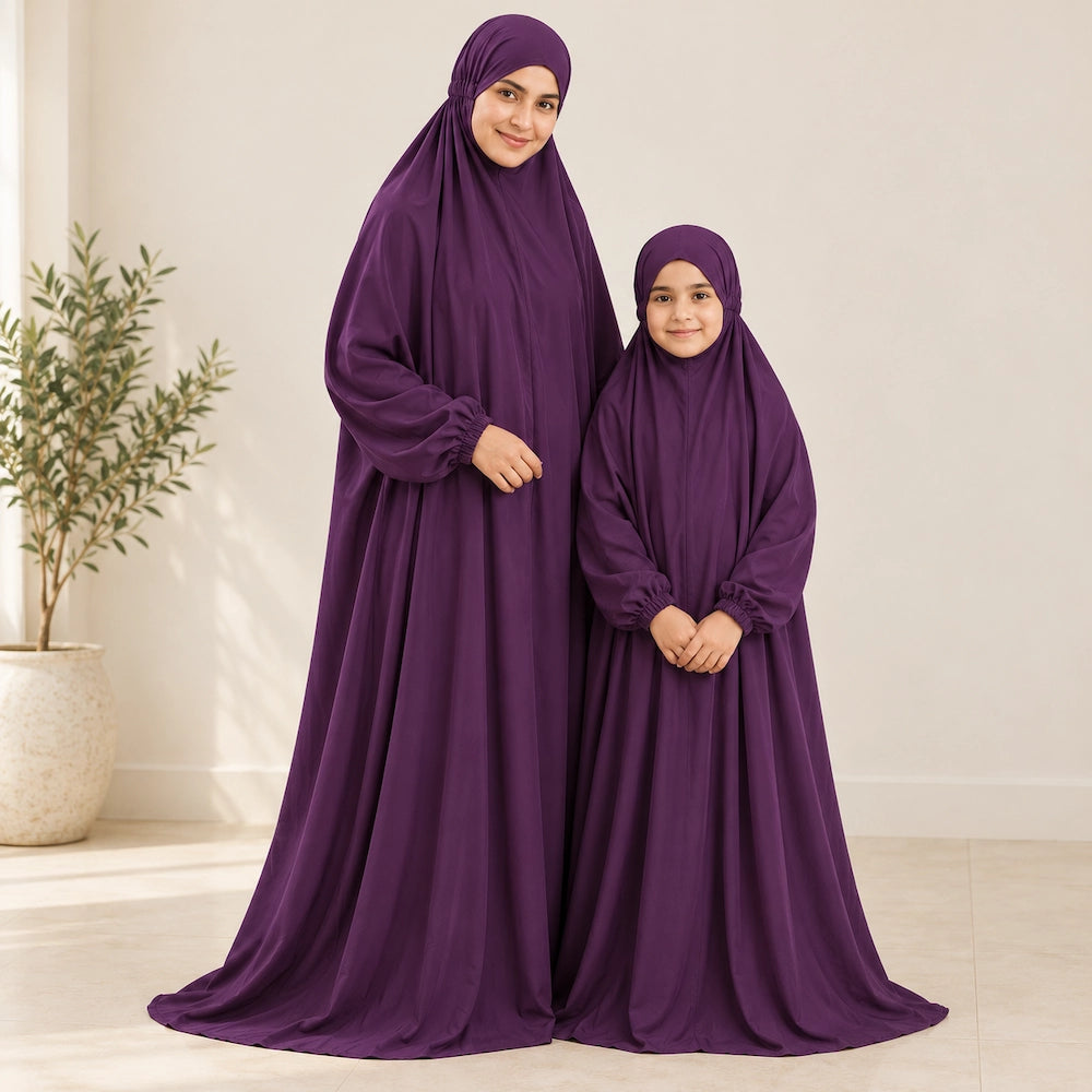 Mother and daughter in matching deep purple plain namaz chaddars with gathered wrist cuffs in a cream interior.