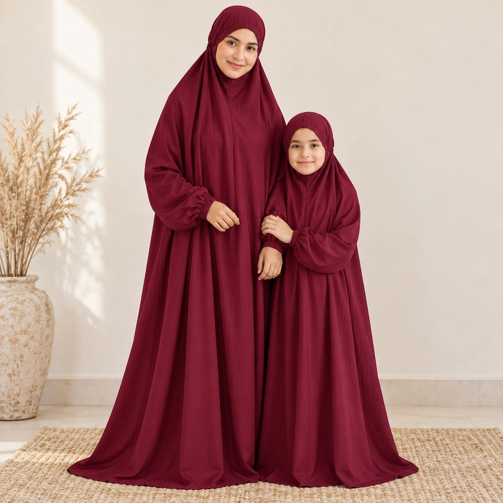 Girl holding her mother's forearm while both wear plain maroon namaz chaddars with elasticated wrists.