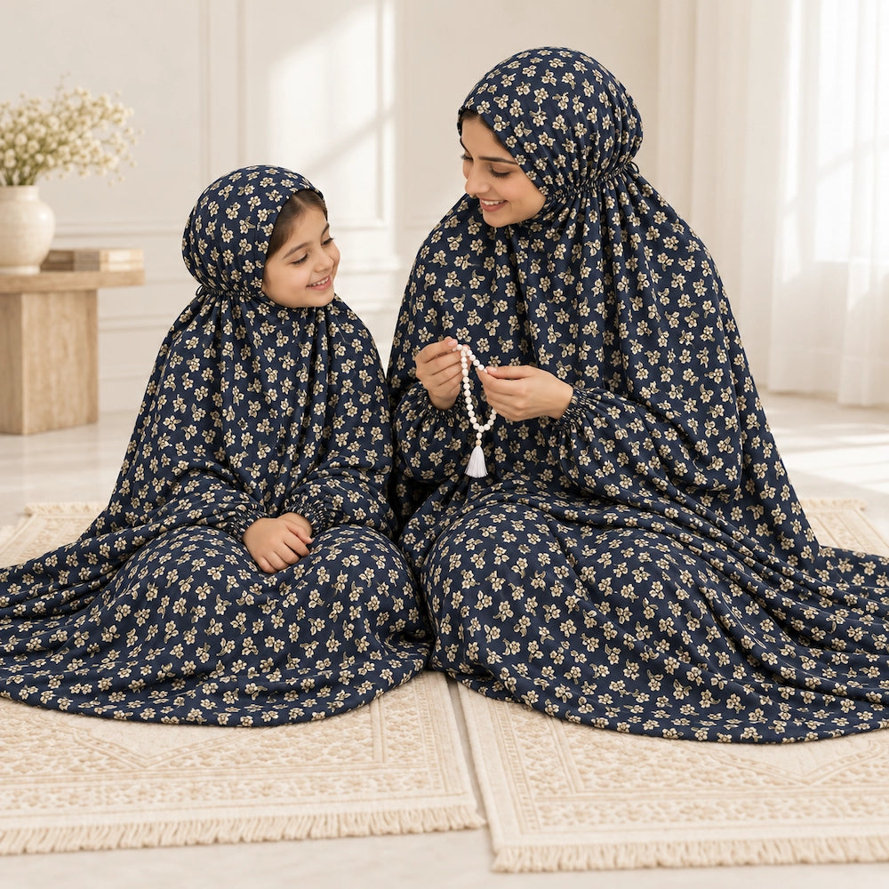 Mother holding prayer beads beside her daughter, both wearing navy blue namaz chaddars with small cream floral sprigs.