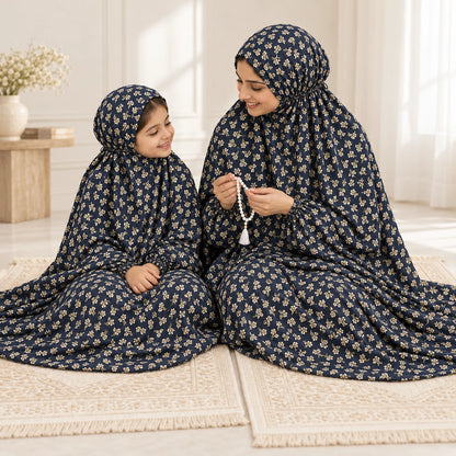 Mother holding prayer beads beside her daughter, both wearing navy blue namaz chaddars with small cream floral sprigs.