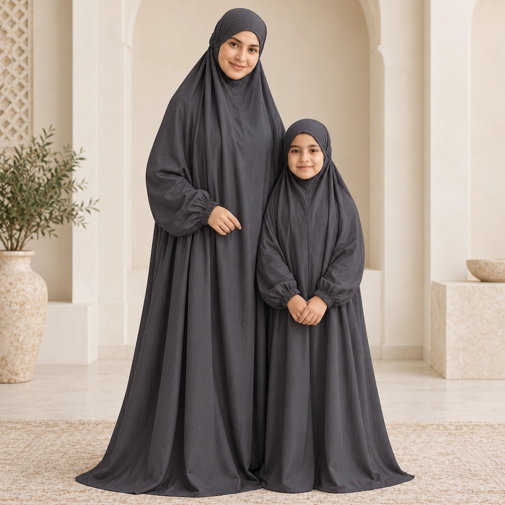 Mother and daughter wearing matching charcoal grey full-length prayer chaddars in a light stone interior.