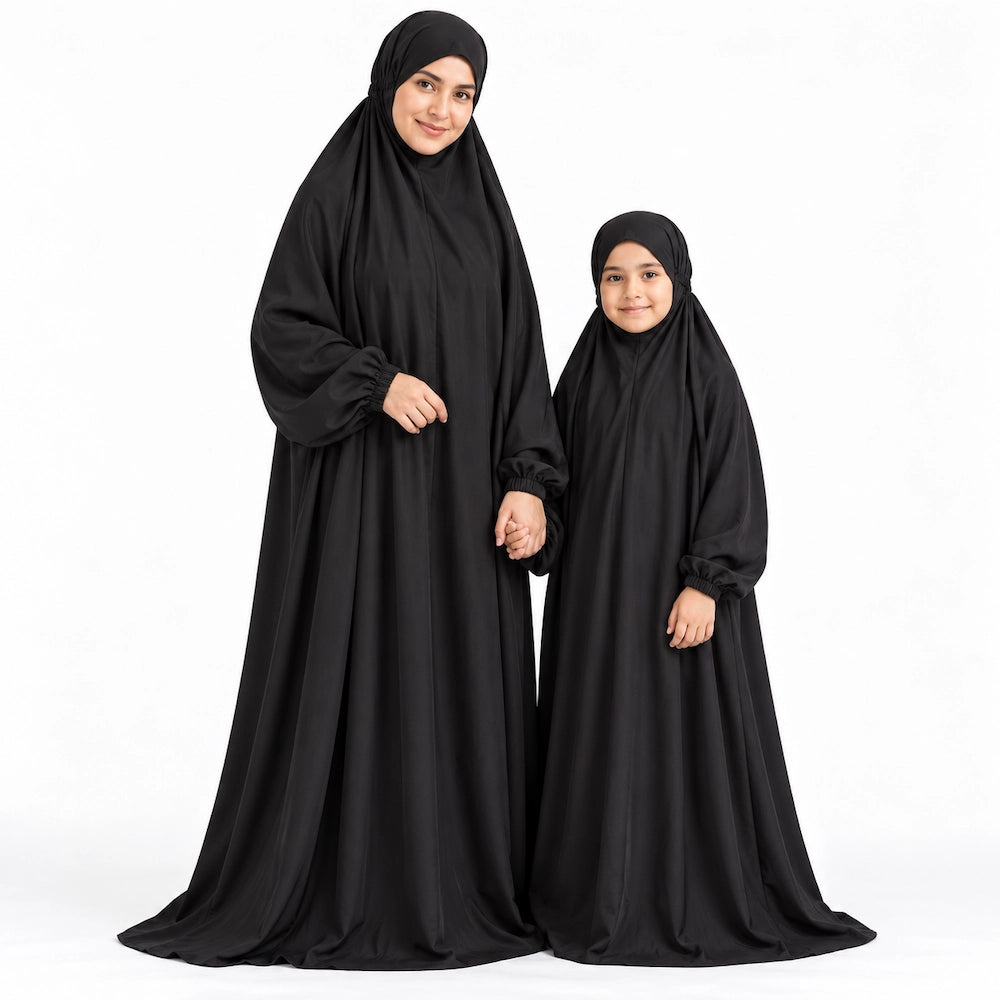 Mother and daughter holding hands in matching plain black full-length namaz chaddars against a white background.