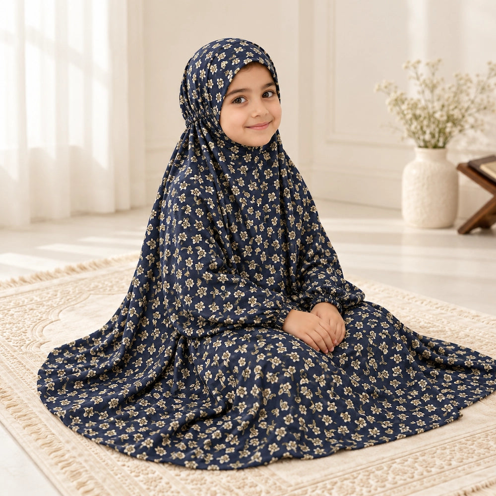 Girl wearing a navy blue prayer chaddar with tiny cream floral motifs and elasticated sleeves on an ivory prayer mat.