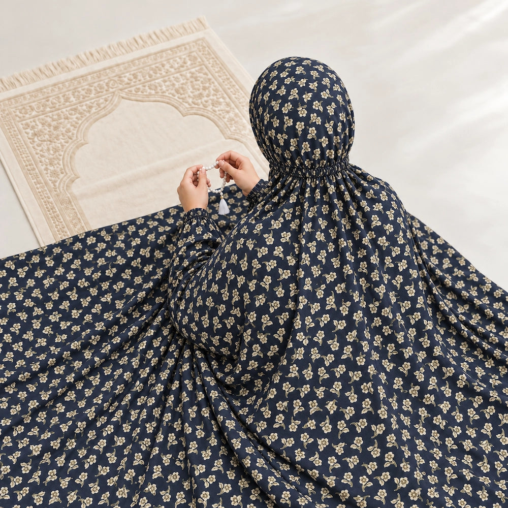 Navy blue floral namaz chaddar draped around a seated woman, showing small cream flower motifs and elastic at the back of the head.