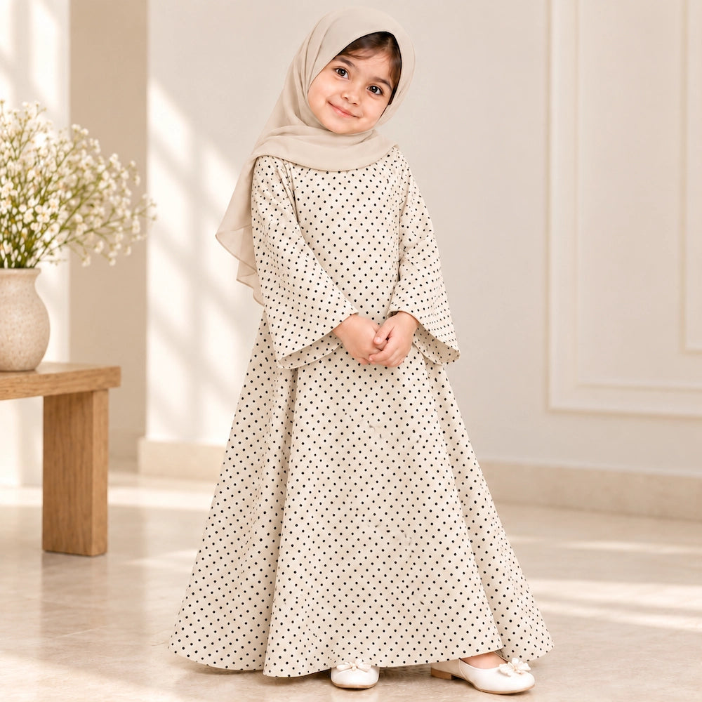 Girl wearing a cream abaya with tiny black polka dots, wide bell sleeves and a flared hem, styled with a cream hijab.