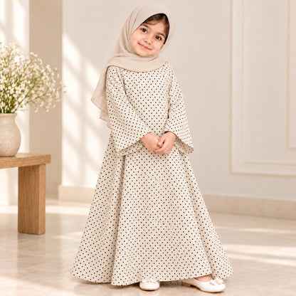 Girl wearing a cream abaya with tiny black polka dots, wide bell sleeves and a flared hem, styled with a cream hijab.