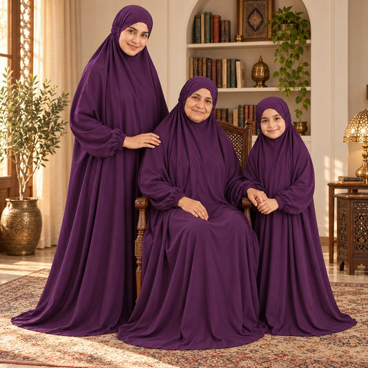 Grandmother seated in a wooden chair with her daughter and granddaughter beside her, all wearing deep purple namaz chaddars.