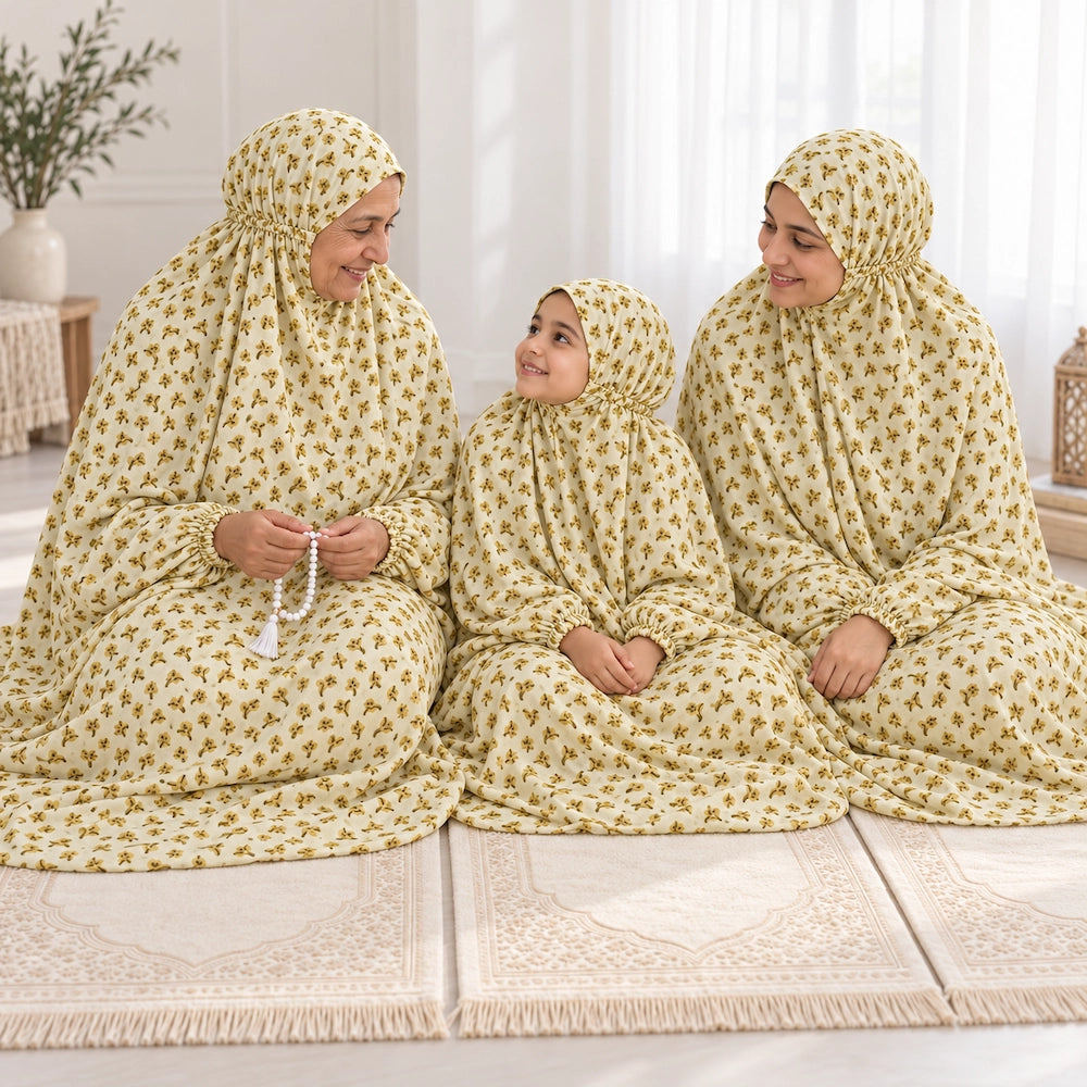 Grandmother, mother and young daughter sitting together in light yellow floral namaz chaddars with matching elasticated sleeves.