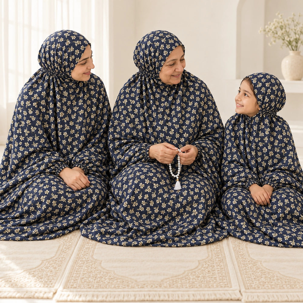 Grandmother seated between her adult daughter and granddaughter in matching navy blue floral namaz chaddars on prayer mats.