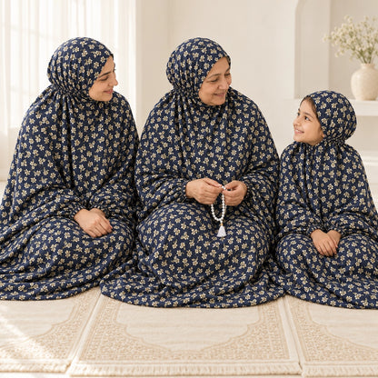 Grandmother seated between her adult daughter and granddaughter in matching navy blue floral namaz chaddars on prayer mats.
