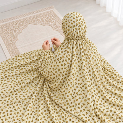 Woman holding prayer beads in a light yellow namaz chaddar with tiny mustard floral sprigs and narrow elasticated wrist cuffs.