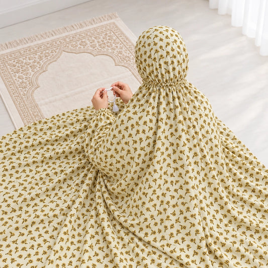 Woman holding prayer beads in a light yellow namaz chaddar with tiny mustard floral sprigs and narrow elasticated wrist cuffs.