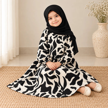 Black and cream kids abaya laid flat, showing oversized abstract flowers, a round neckline, elastic cuffs and a flared hem.