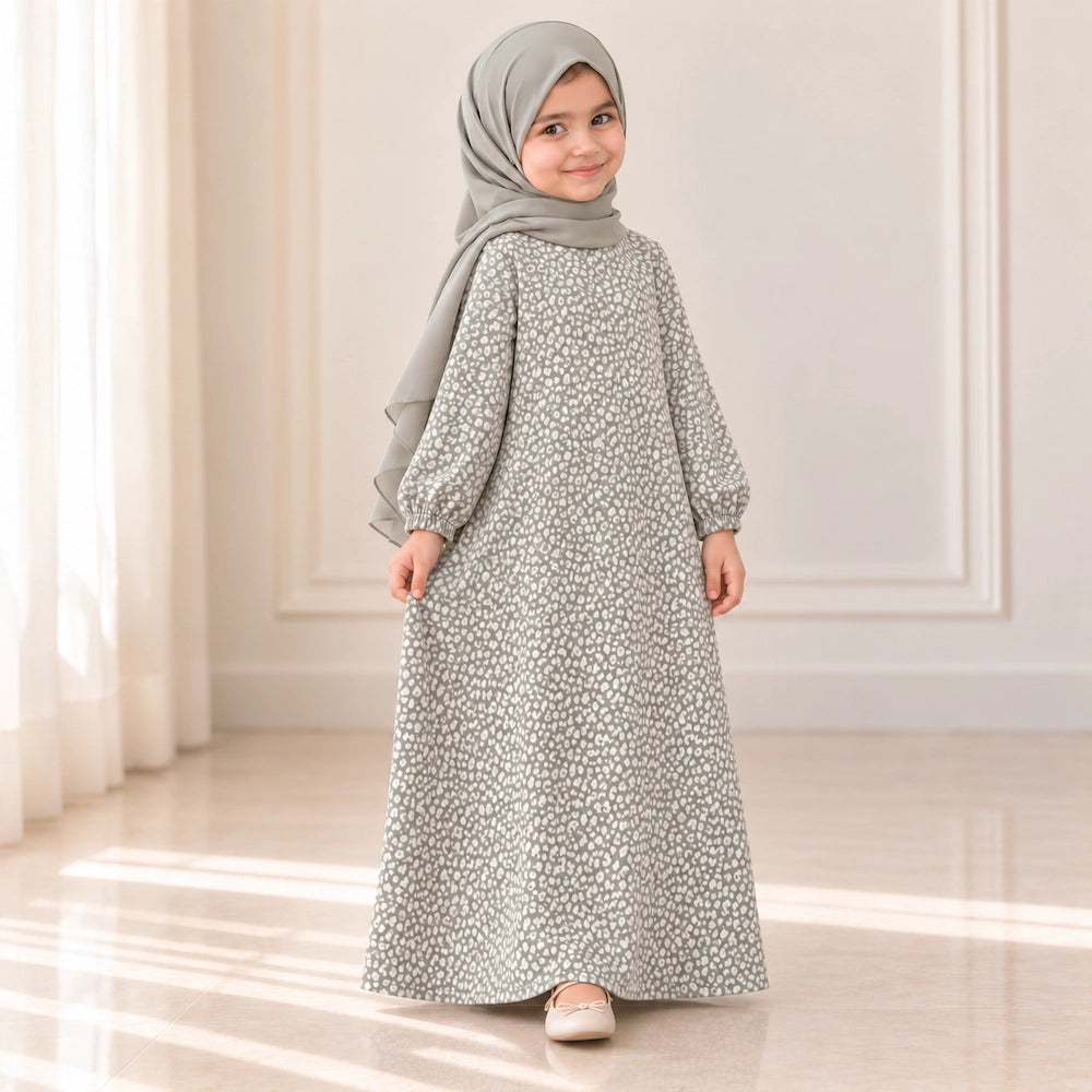 Light grey girls' abaya laid flat with a small ivory speckled print, round neckline, gathered cuffs and flared shape.